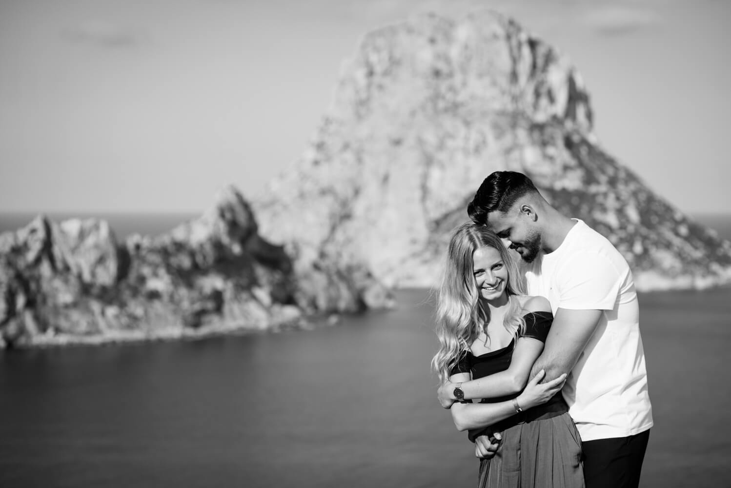 black and white photo of a couple cuddling by the sea