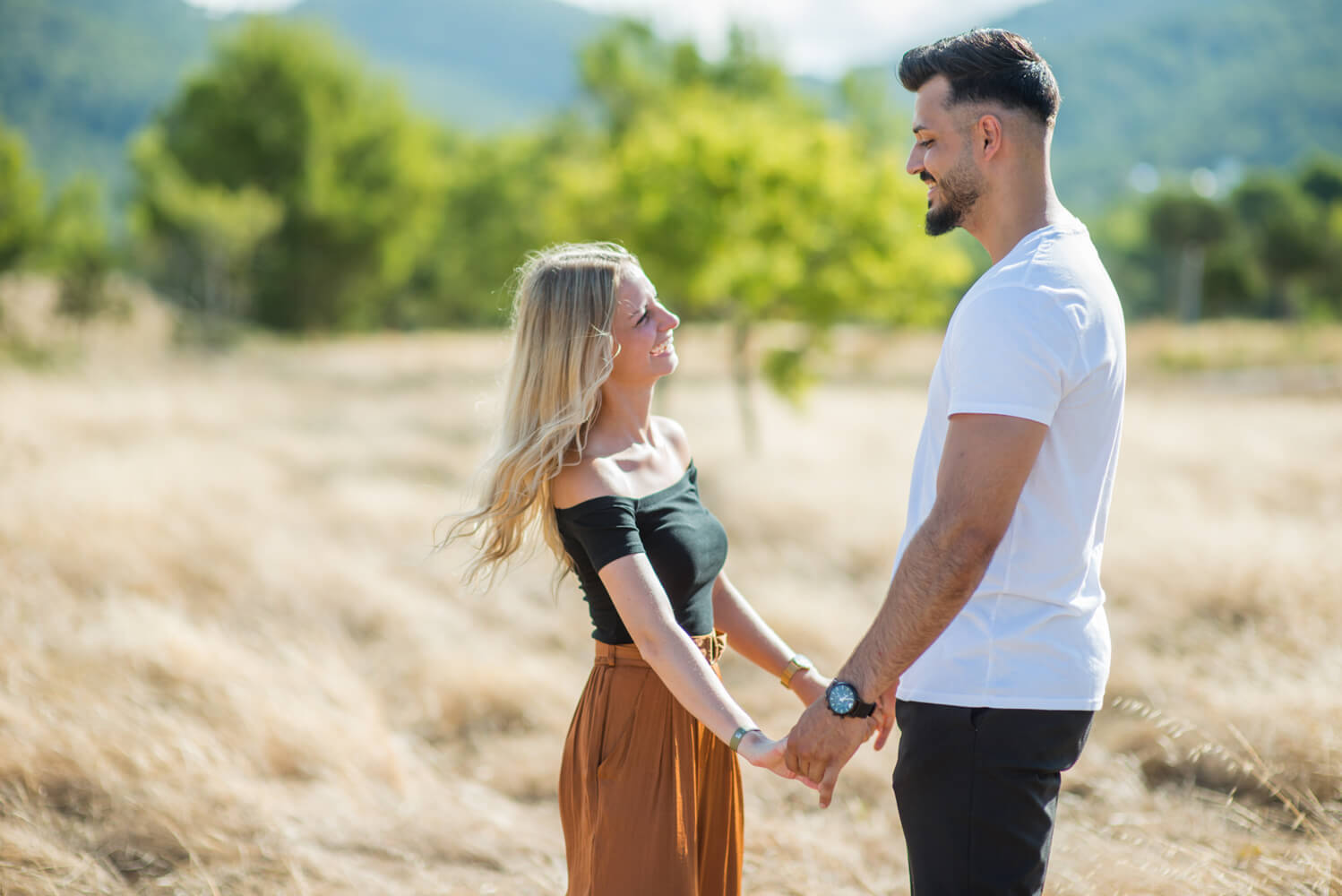 couple holding hands and smiling at eachother in a field