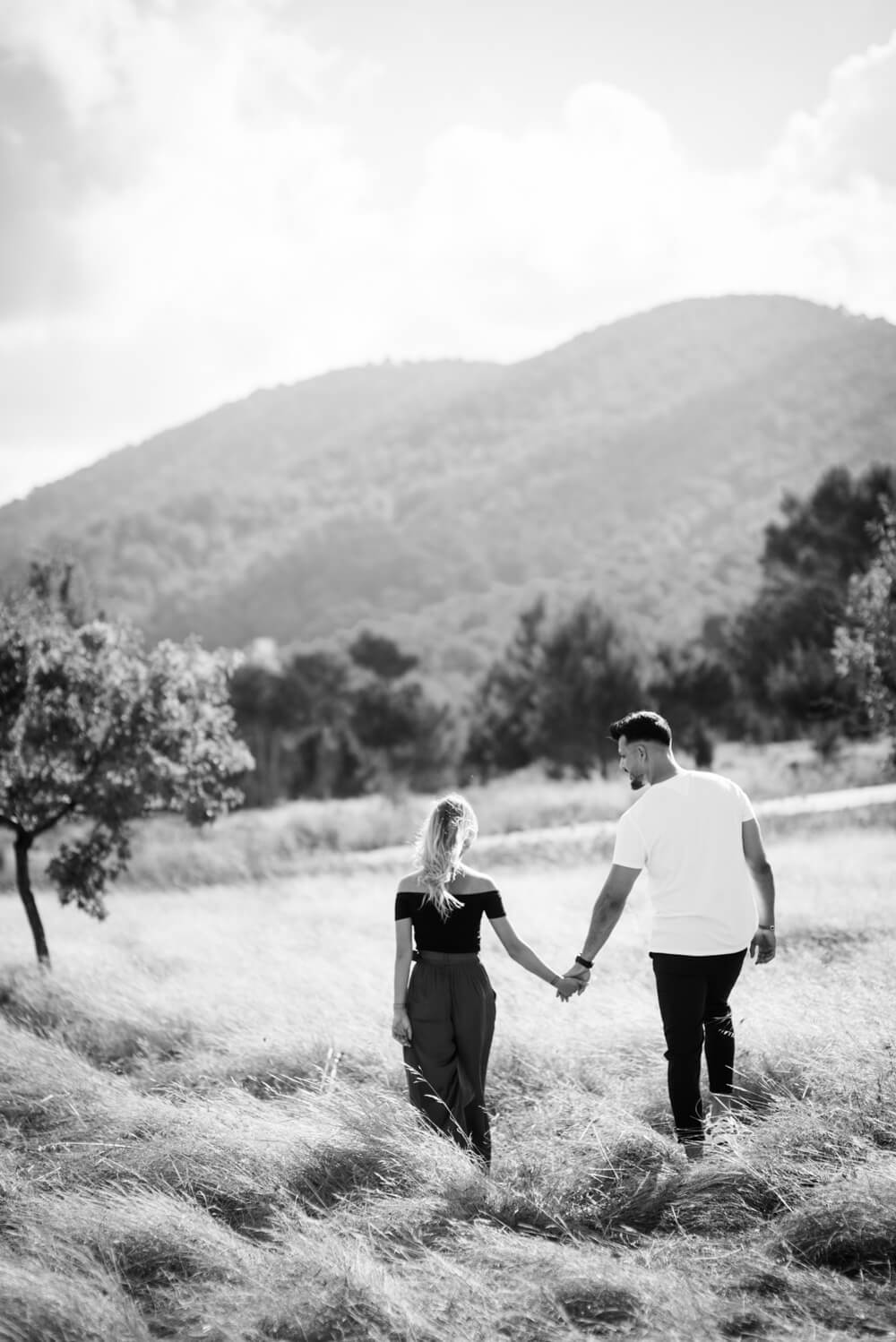 a couple walking through a field towards the hills holding hands