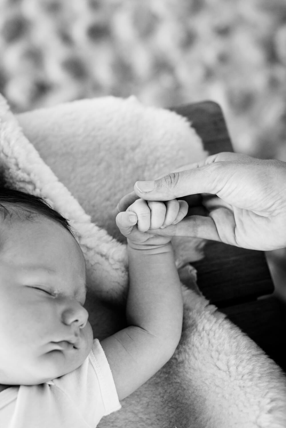 black and white image of a sleeping newborn baby holding hands with his mother