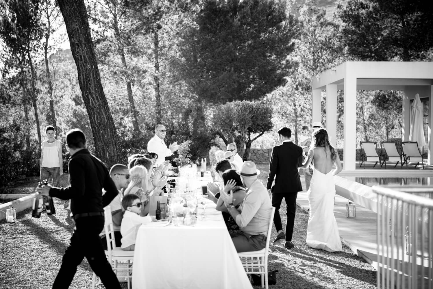 black and white photograph of guests seated at a long table at a wedding in the countryside under pine trees in Ibiza