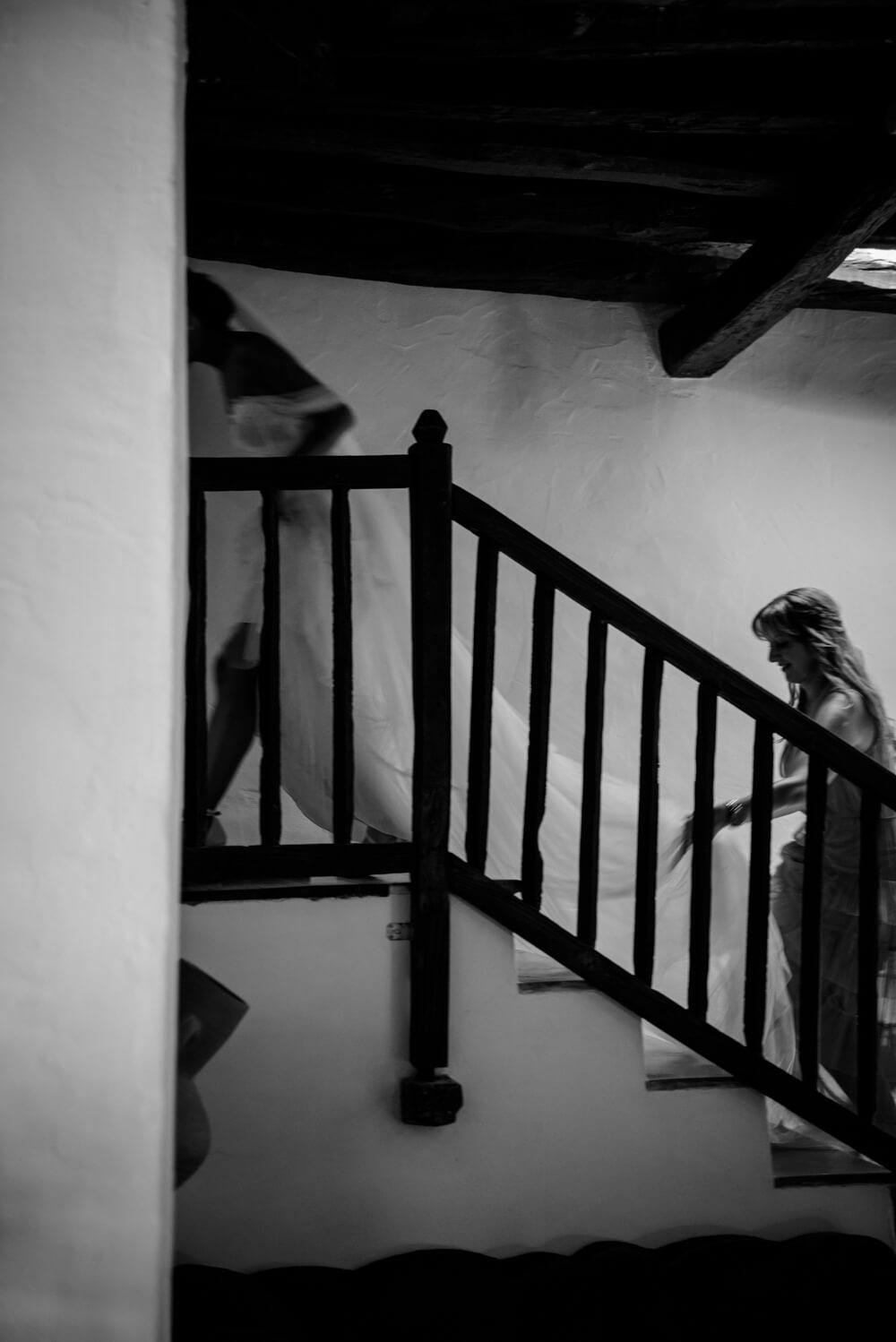 bride climbing the stairs with bridesmaid holding veil at an Ibiza wedding, black and white photo