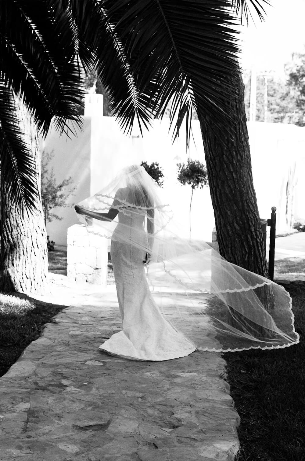black and white photograph of the view from behind a bride in her wedding dress with her veil blowing in the wind