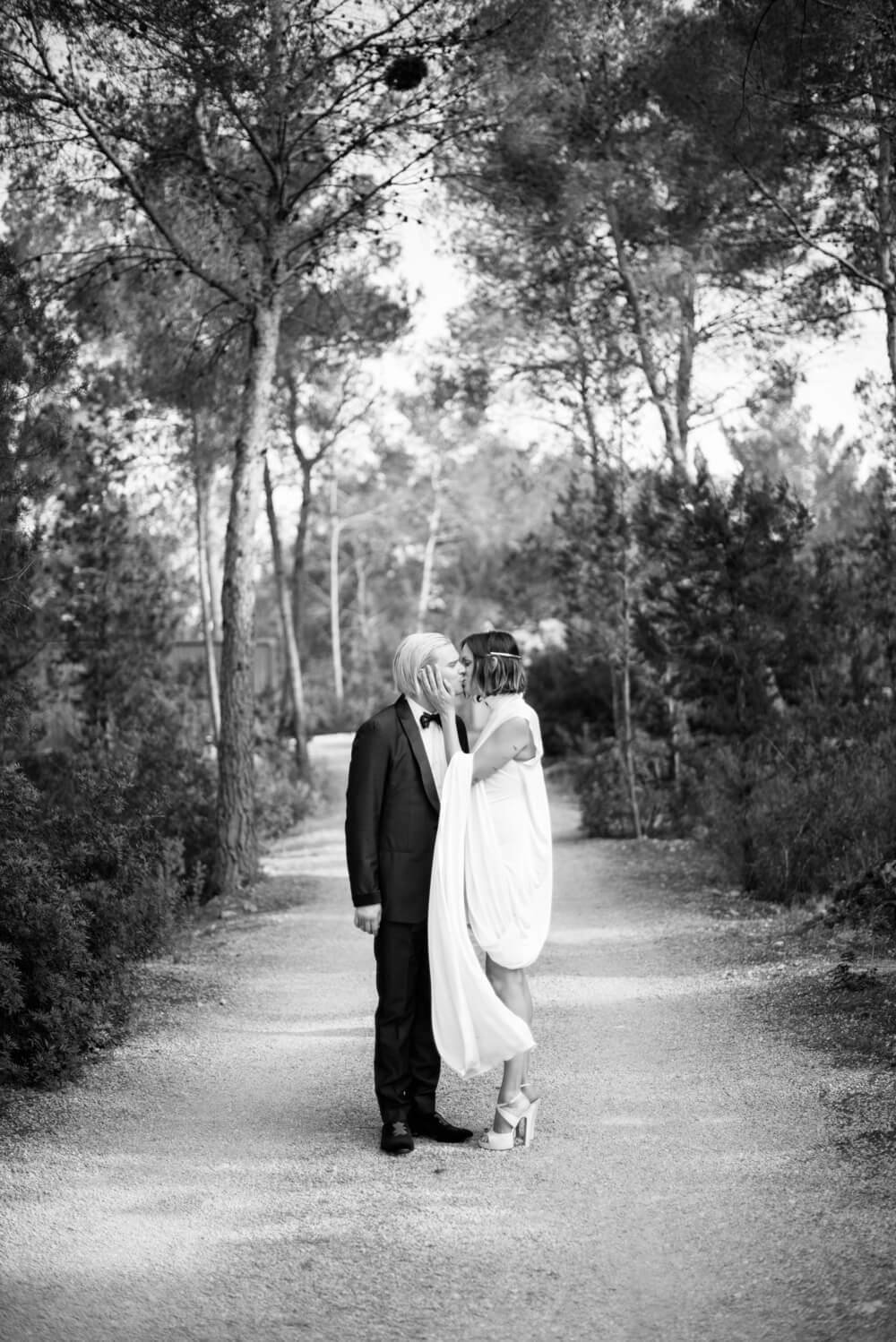 black and white photograph of a couple kissing at their Ibiza wedding on a dirt track in a pine forest
