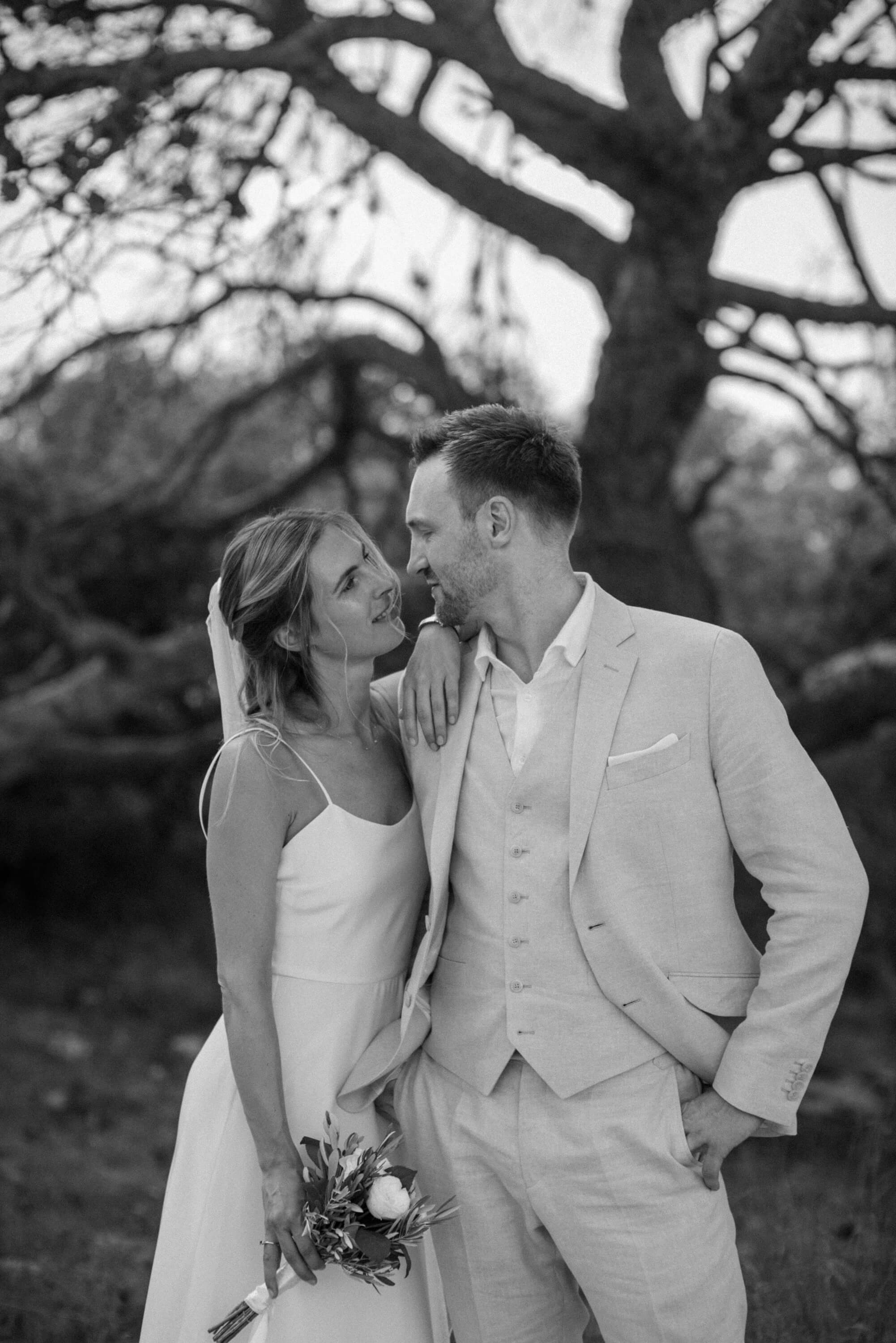 Couple look at eachother with love just before their wedding in Ibiza, flowers in hand by the ocean