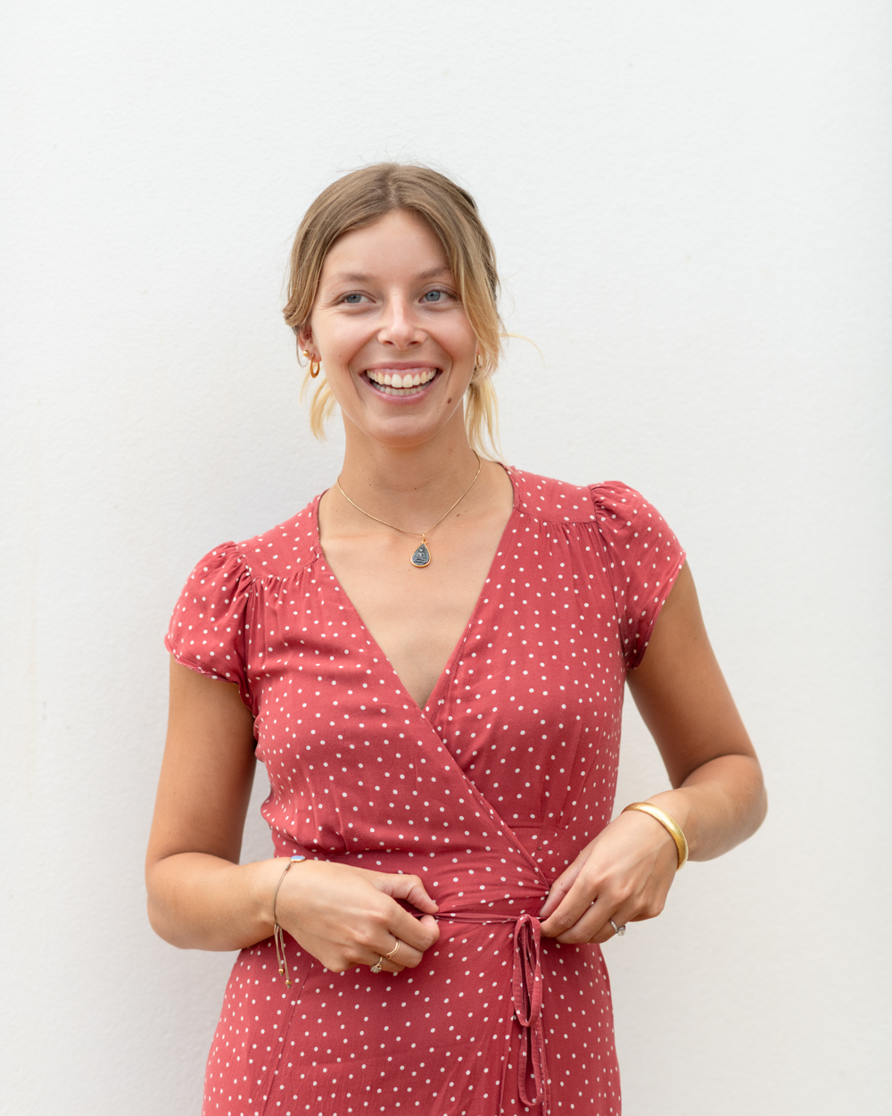 Woman smiling holding her red dress with white polka dots. white wall as the background in ibiza