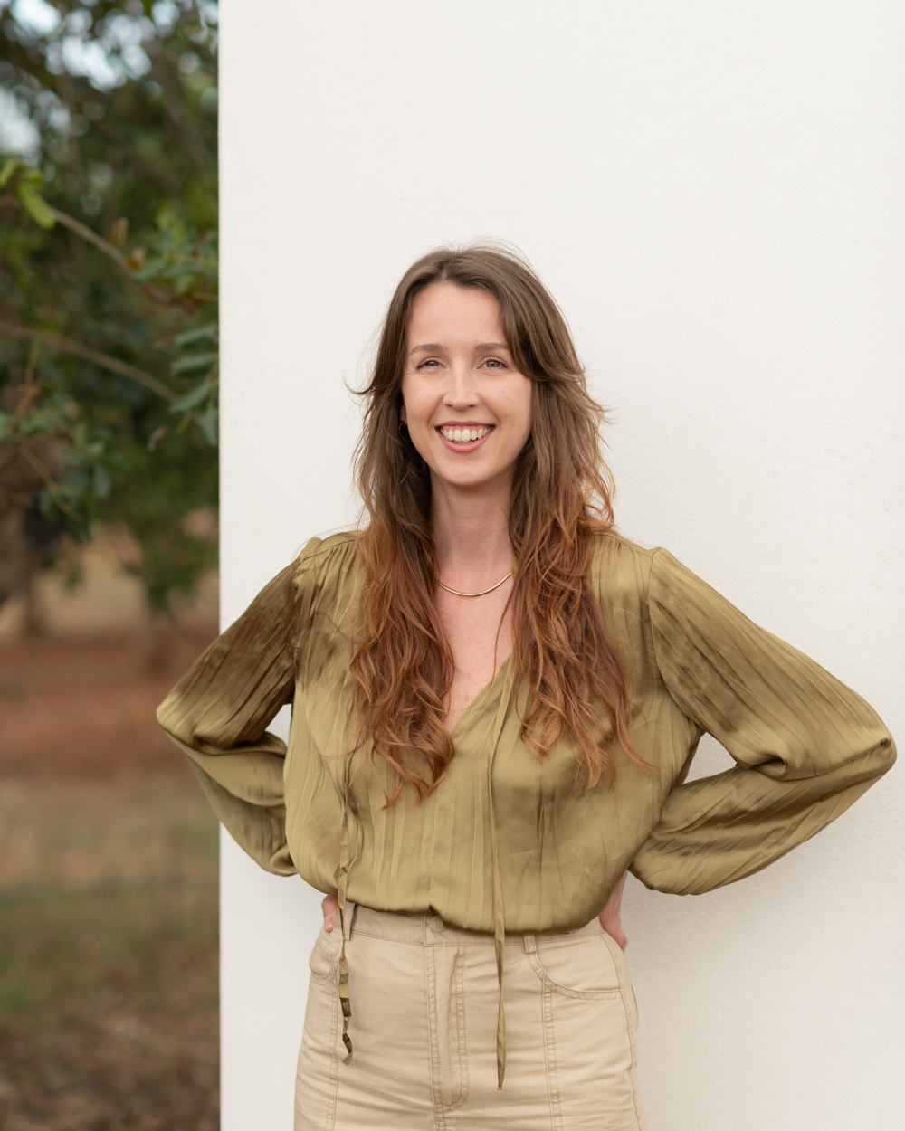 woman standing with white wall as background, strong pose smiling wearing a green shirt. Clarissa Sofia - Ibiza wedding photographer